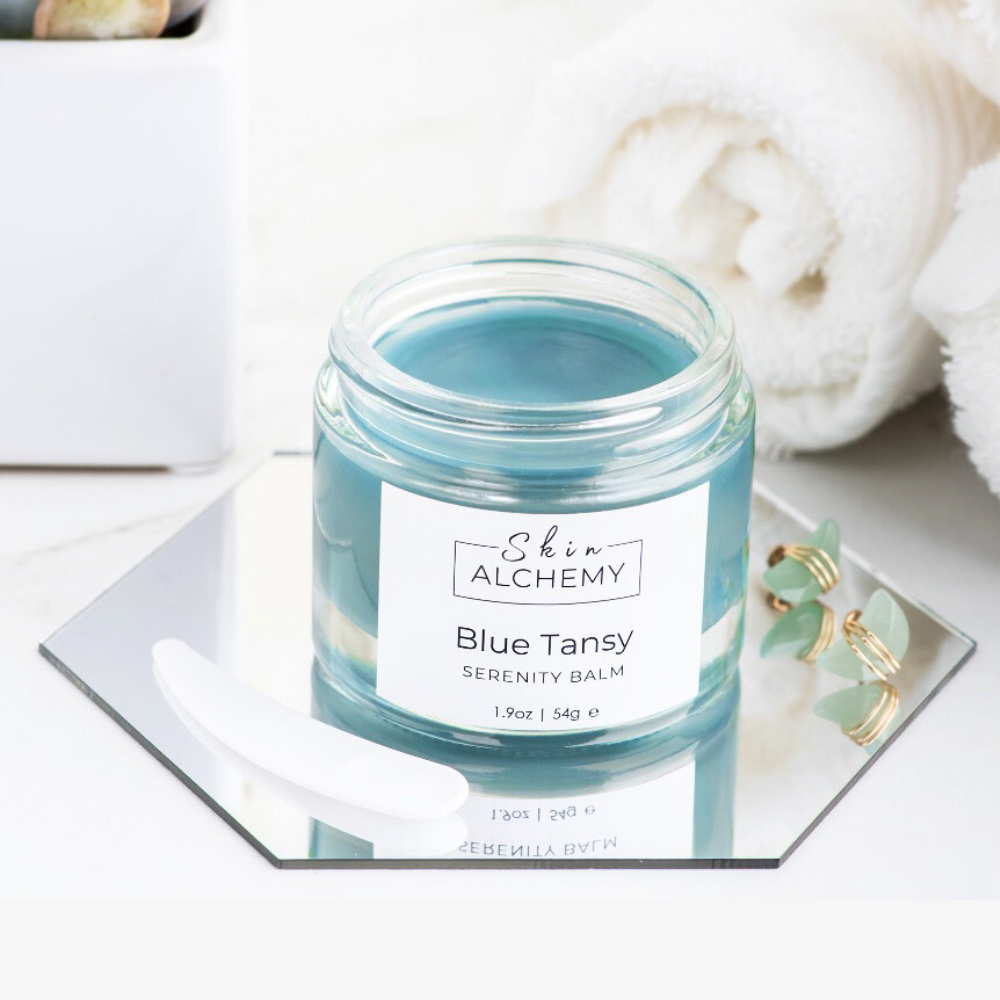 Jar of Blue Tansy Serenity Balm from Skin Alchemy on a white surface with a towel in the background.