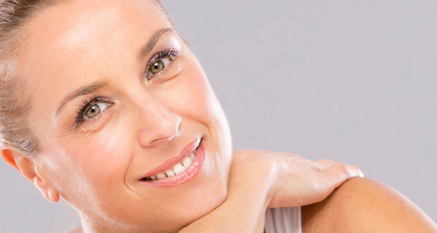 Woman smiling, resting her chin on her arm against a gray background