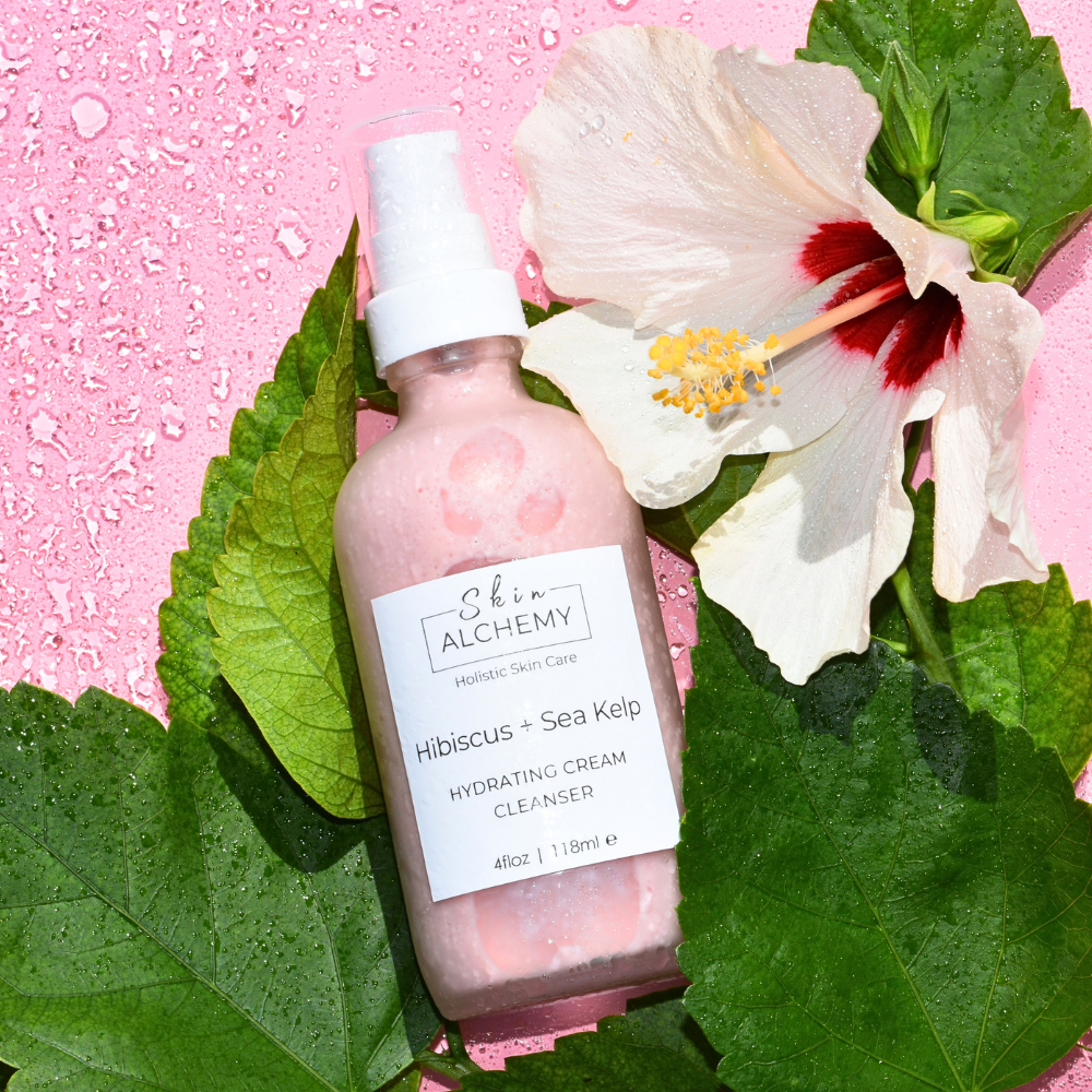 Skincare bottle labeled 'Alchemy' with a flower and leaves on a pink background